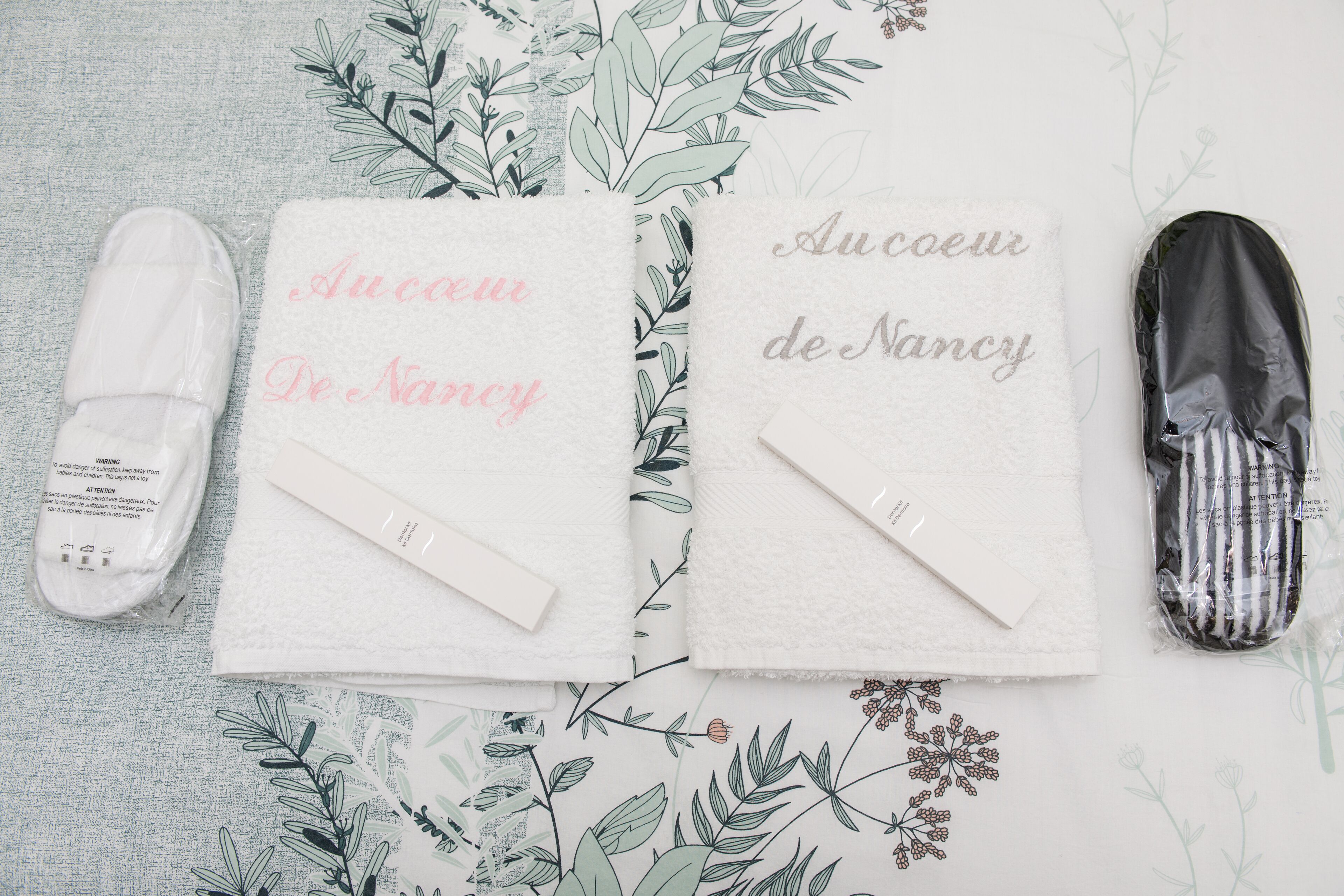 Une serviette ornée de la mention « Au cœur de Nancy » et une paire de chaussons posés sur une surface à motifs.