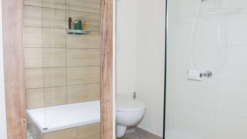 A bathroom with a shower, toilet, and a shelf with toiletries.