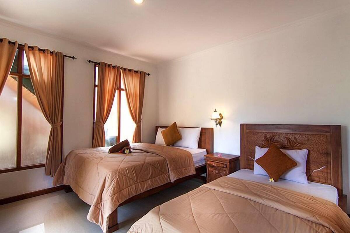 A hotel room with two beds, a nightstand, a lamp, and curtains.