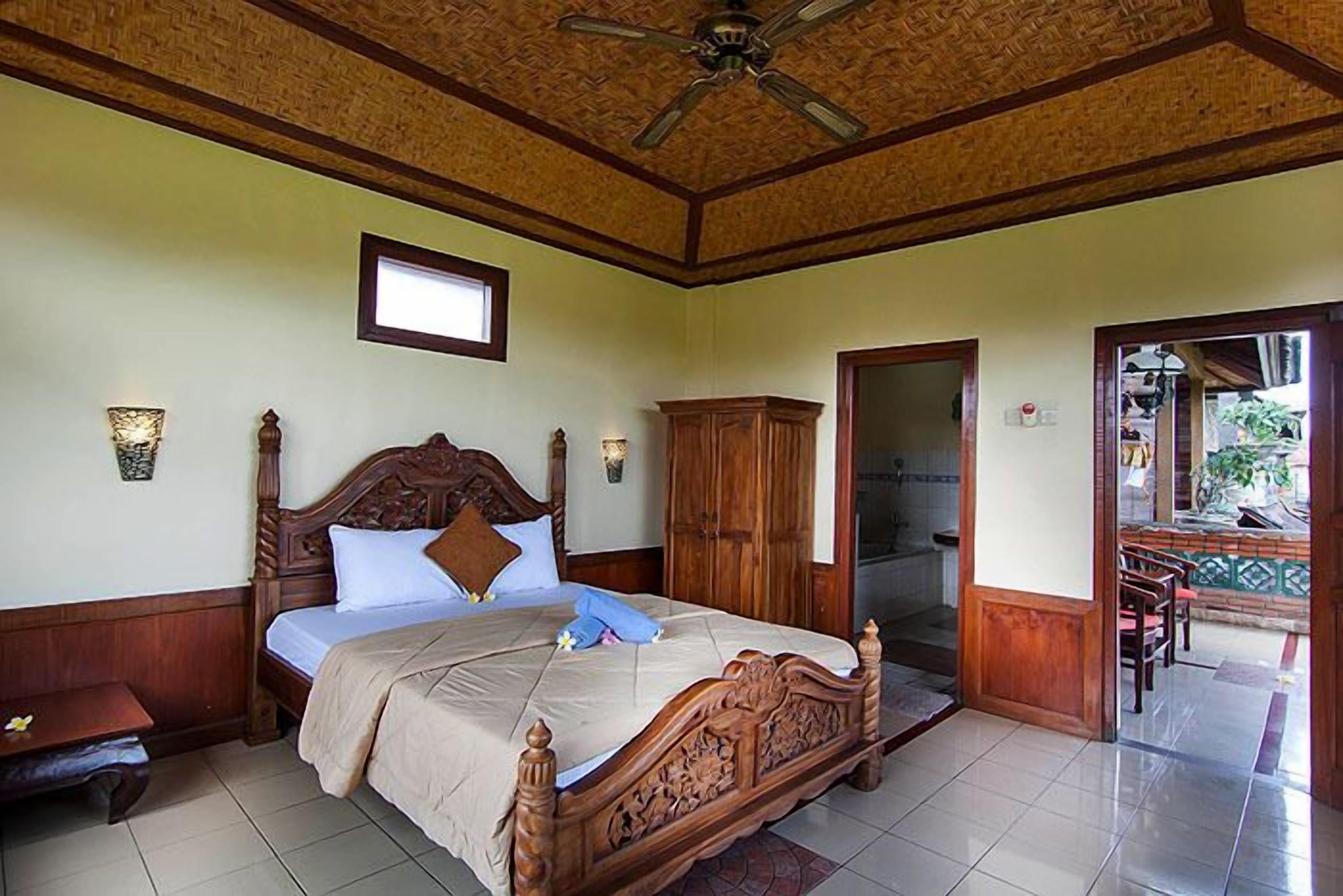 A bedroom with a wooden bed, a ceiling fan, a window, and a view of the outside.