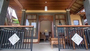A wooden balcony with a railing, a bed, and a small table in the background. - Ganesha Ubud Inn (Ubud)