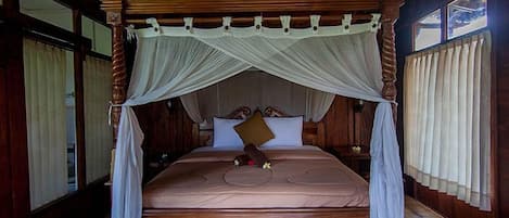 Una cama grande y ornamentada de madera con dosel, un ventilador de techo y cortinas en las ventanas.
