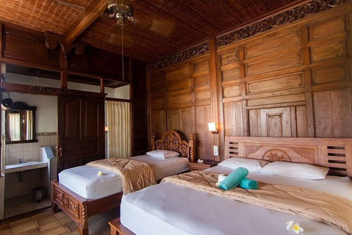 A room with two wooden beds, a wooden wardrobe, a mirror, and a small desk with a lamp.