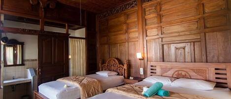 A room with two wooden beds, a wooden wardrobe, a mirror, and a small desk with a lamp.