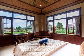 Un dormitorio con una cama grande, cabecero de madera y varias ventanas que ofrecen vistas a zonas verdes y edificios.