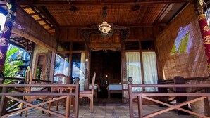 A traditional wooden structure with a thatched roof, wooden furniture, and a central chandelier. - Ganesha Ubud Inn (Ubud)