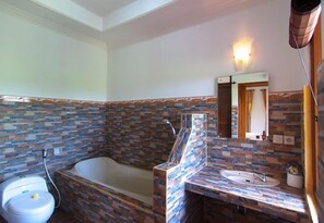 Un baño con salpicadero de mosaico de piedra, una bañera independiente, un lavabo con espejo y una lámpara de pared.