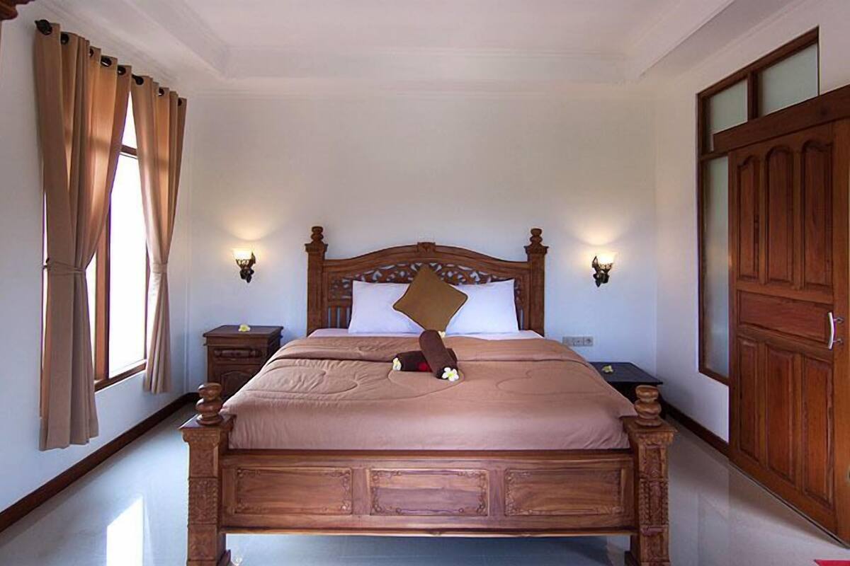 A neatly made bed with a wooden headboard, two bedside tables with lamps, and a large wooden wardrobe.