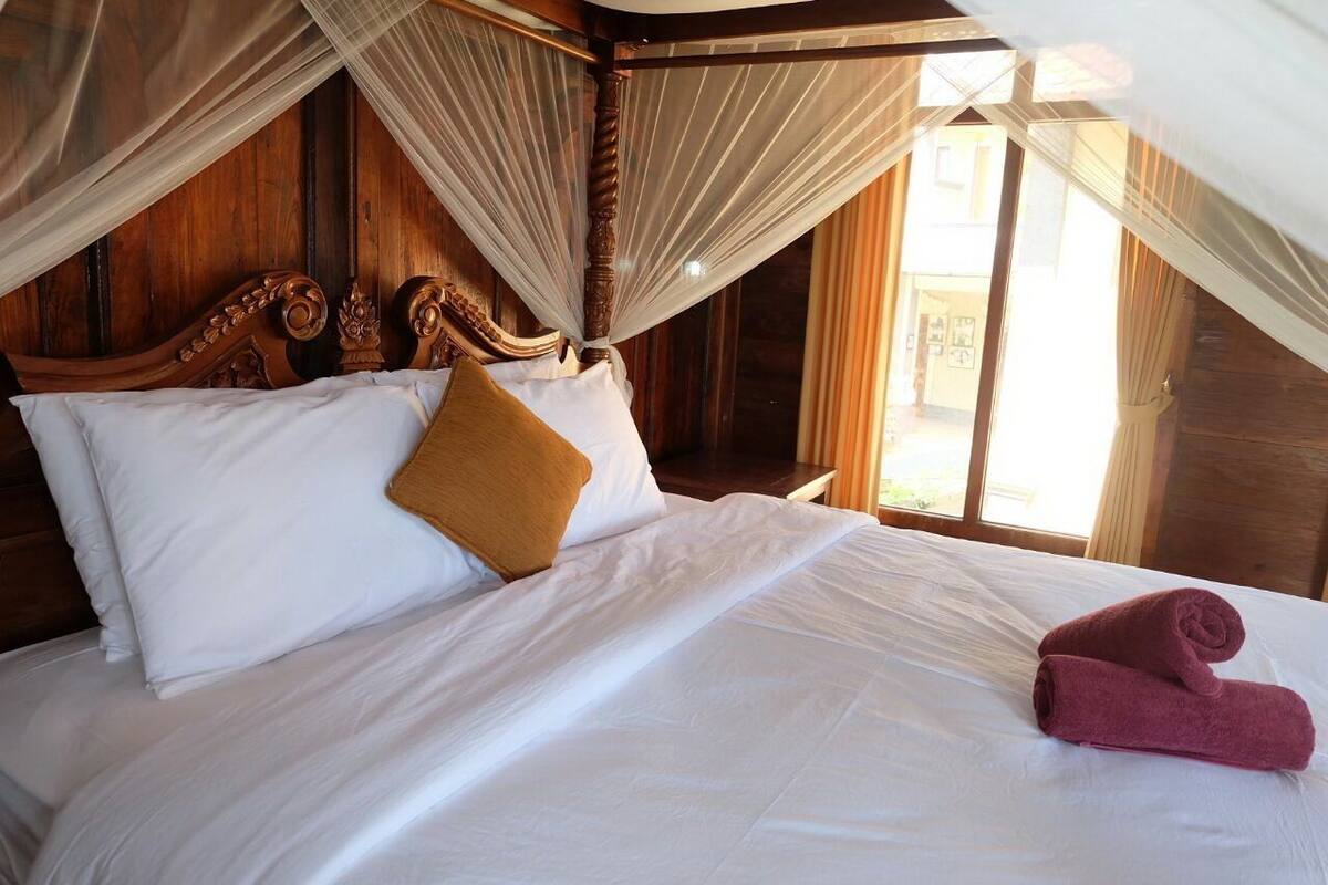 A bed with white linens, a brown pillow, and a rolled-up towel.