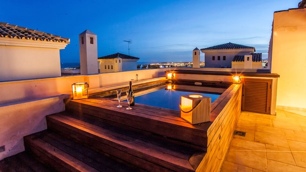 A rooftop pool area with steps leading down to a pool, surrounded by buildings and a clear sky. - Medina Luxury Penthouse (Marbella)