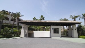 A gated entrance with a covered walkway, palm trees, and a building with a tiled roof. - Medina Luxury Penthouse (Marbella)
