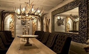 A dining area with a long table, upholstered chairs, a chandelier, and a mirror with a decorative frame. - Hovde Gård (Orland)