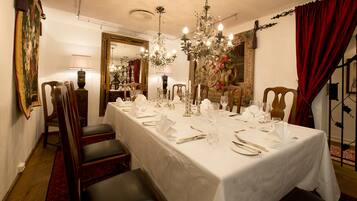 A formal dining room with a long table set for a meal, surrounded by chairs, a chandelier, and a large mirror.