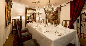 A formal dining room with a long table set for a meal, surrounded by chairs, a chandelier, and a large mirror.