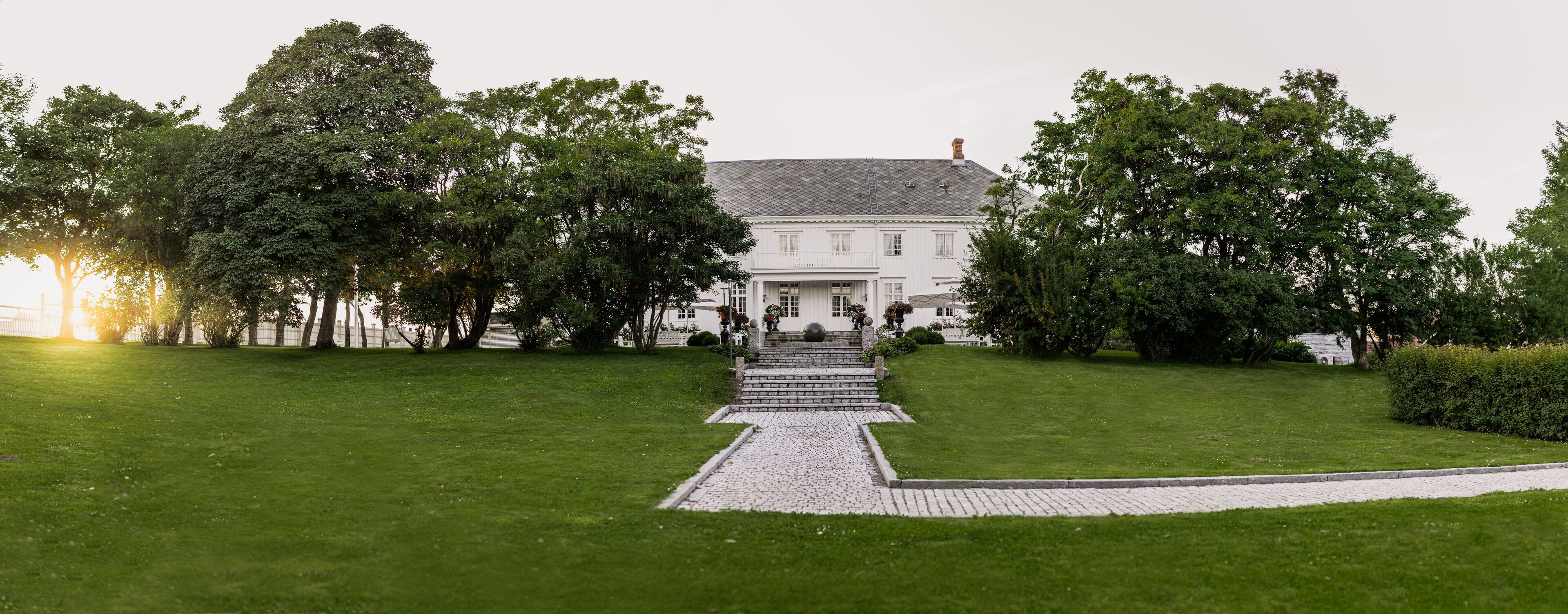 A white building with a symmetrical facade, a central entrance with steps, and a paved pathway leading to it.