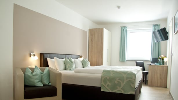 Ein modernes Hotelzimmer mit einem großen Bett, einer Couch, einem Schreibtisch mit einem Laptop und einem Fernseher an der Wand.