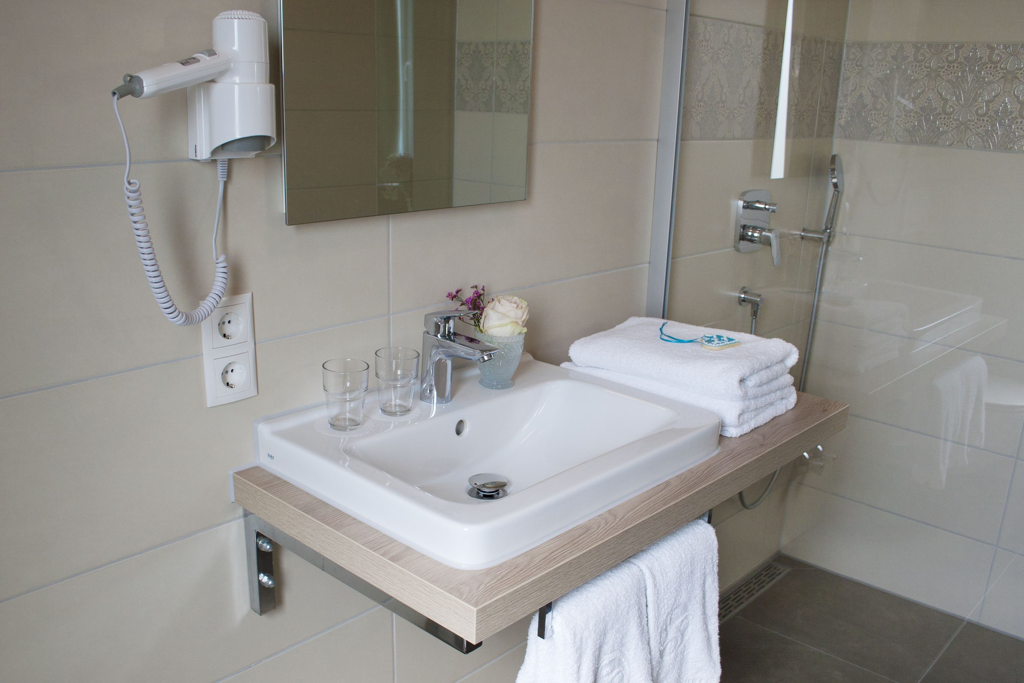 A bathroom with a sink, mirror, and a hairdryer mounted on the wall.