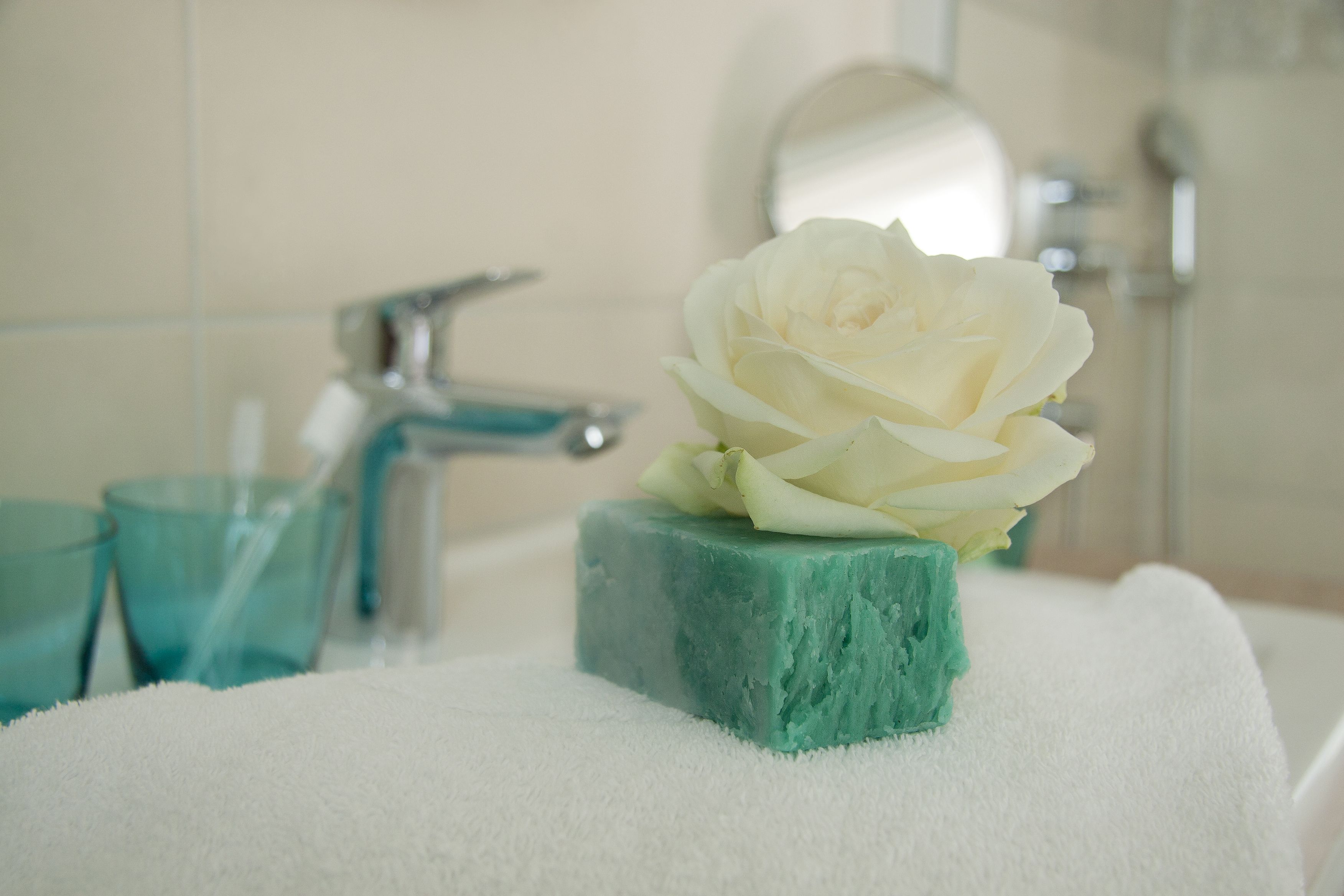Un baño con una pastilla de jabón verde, una toalla blanca y una rosa blanca sobre el jabón.
