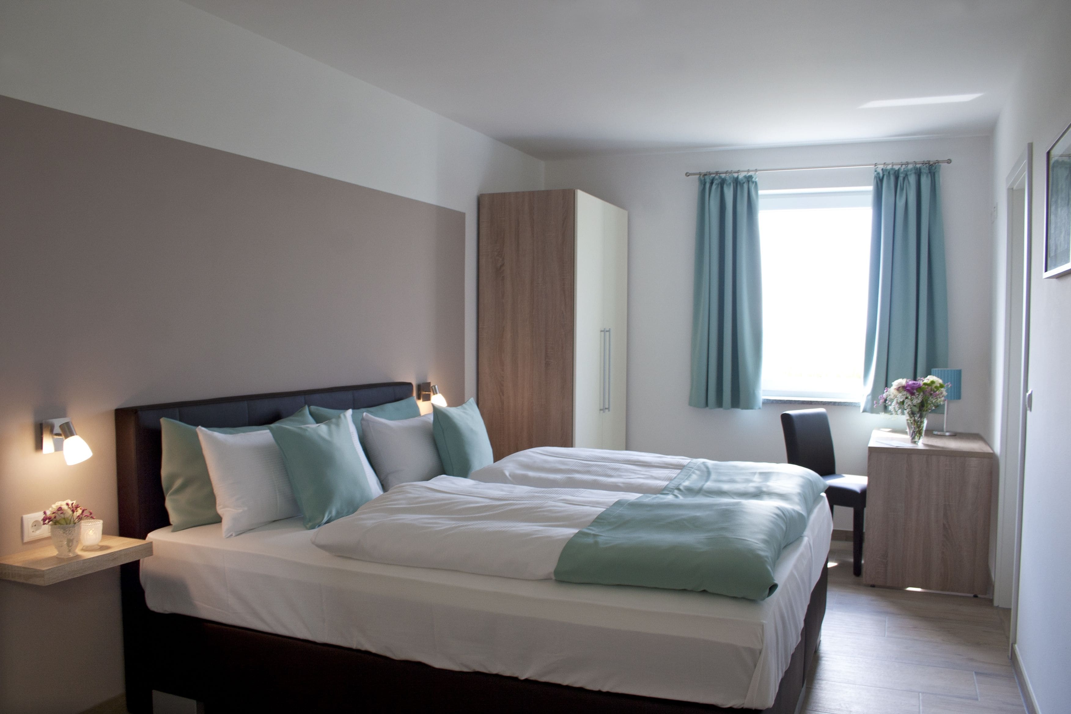 Ein modernes Hotelzimmer mit einem großen Bett, Nachttischen, einem Schreibtisch und einem Fenster mit Vorhängen.