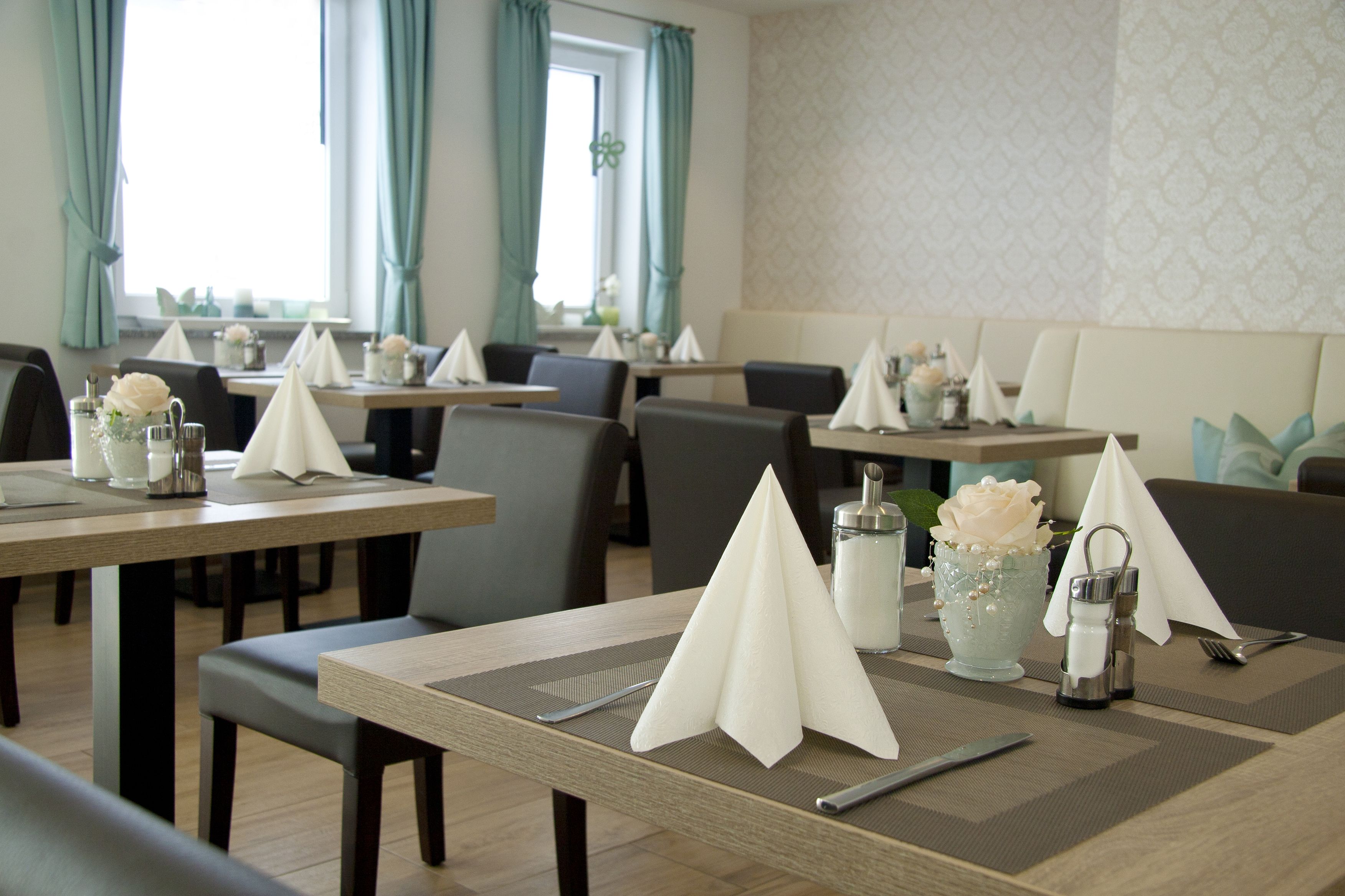 A dining area with tables set for service, featuring placemats, napkins, and a vase with a flower.