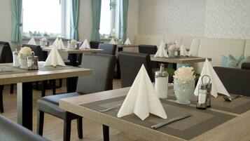A dining area with tables set for service, featuring placemats, napkins, and a vase with a flower.