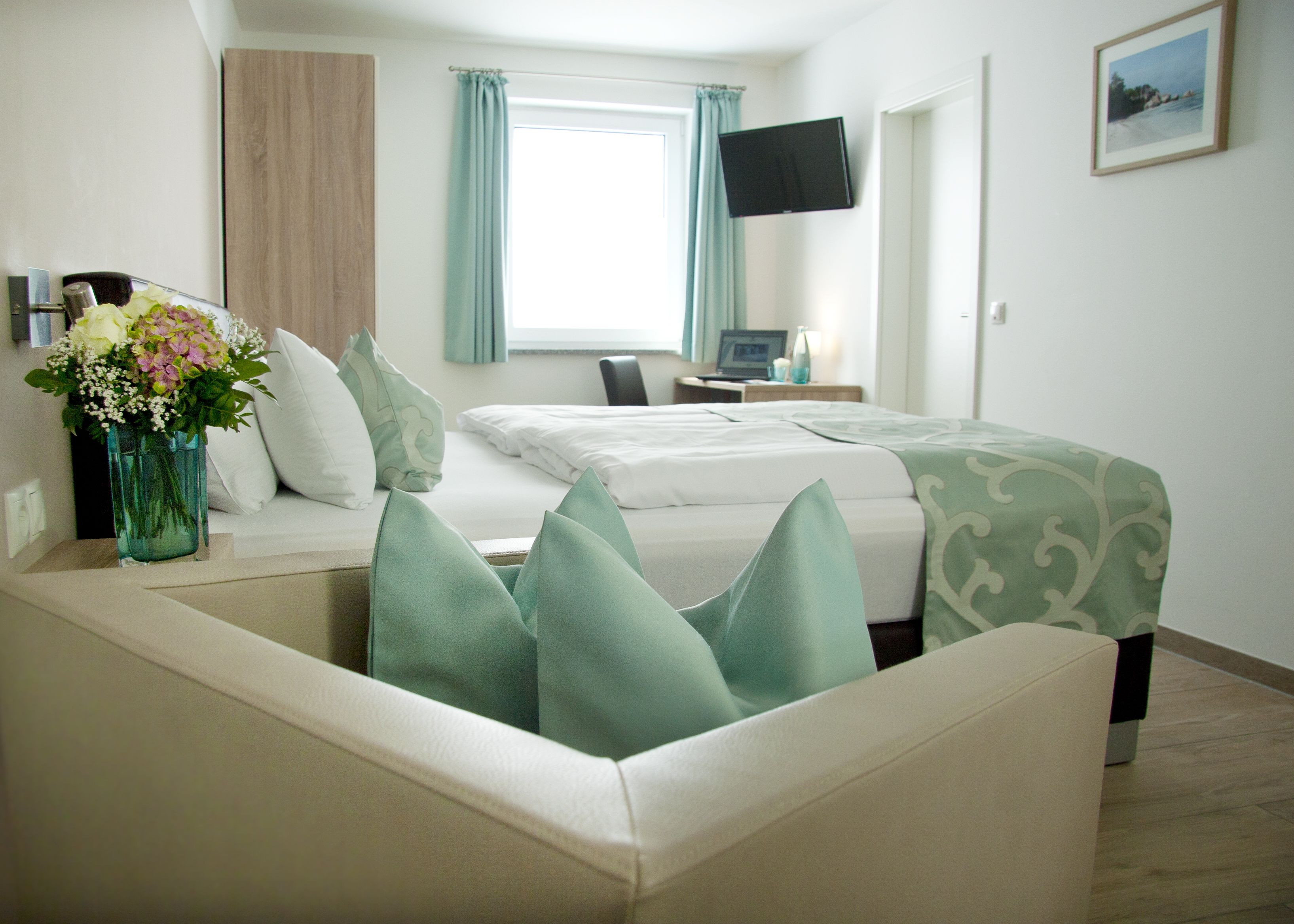 Quarto de hotel com cama, mesa, televisão e janela com cortinas.