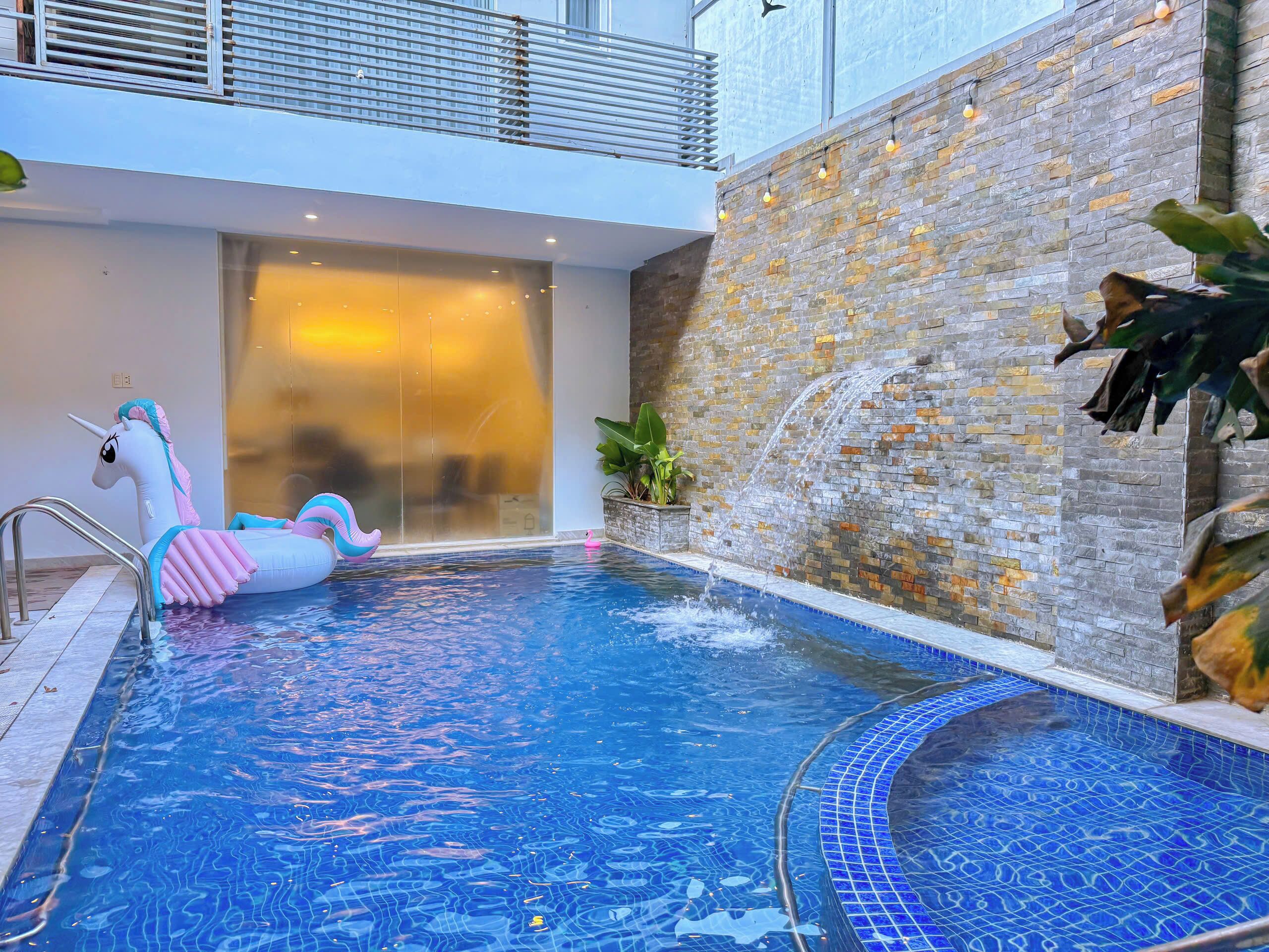 Une piscine intérieure avec un flotteur en forme de licorne, une fontaine et un mur en pierre.