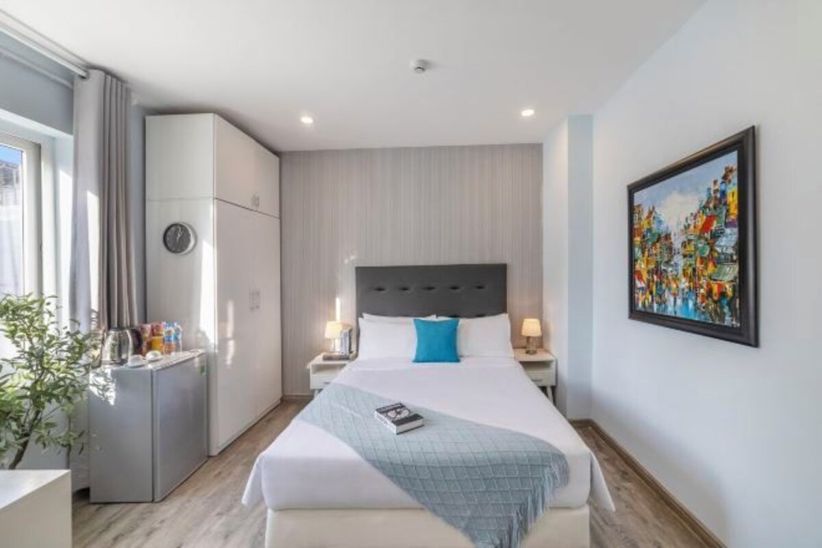 Quarto de hotel moderno com uma cama grande, uma escrivaninha pequena, um frigorífico e um quadro na parede.