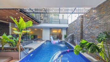 An indoor swimming pool with a fountain, surrounded by plants and a stone wall.