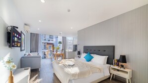 A modern hotel room with a large bed, a bedside table with a lamp, a flat-screen TV mounted on the wall, and a view of the city through large windows. - Hese Boutique Hotel & Apartment (Ho Chi Minh City)