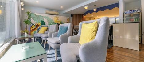A modern hotel lobby with grey armchairs, a glass coffee table, a mural, a bar area, and a minibar.