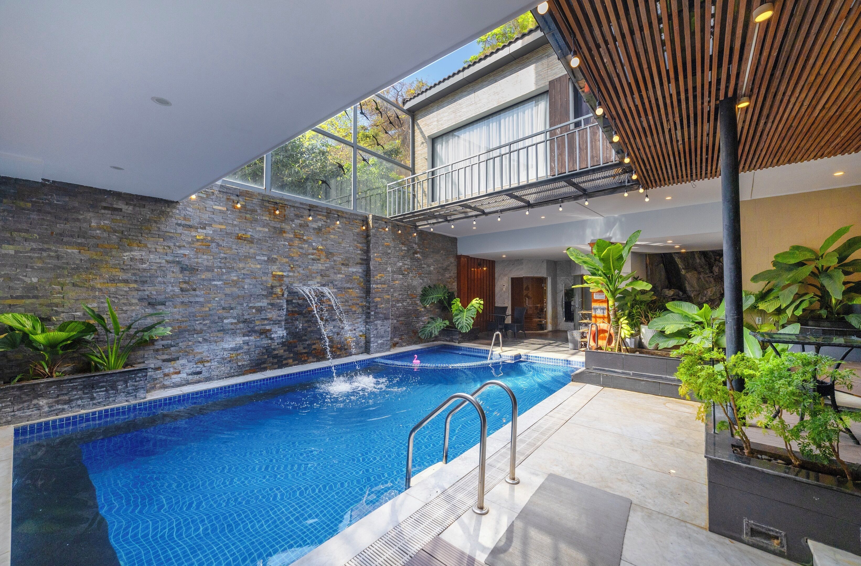 Ein moderner Poolbereich im Innenbereich mit Steinwand, Wasserfall und einer Holzpergola.