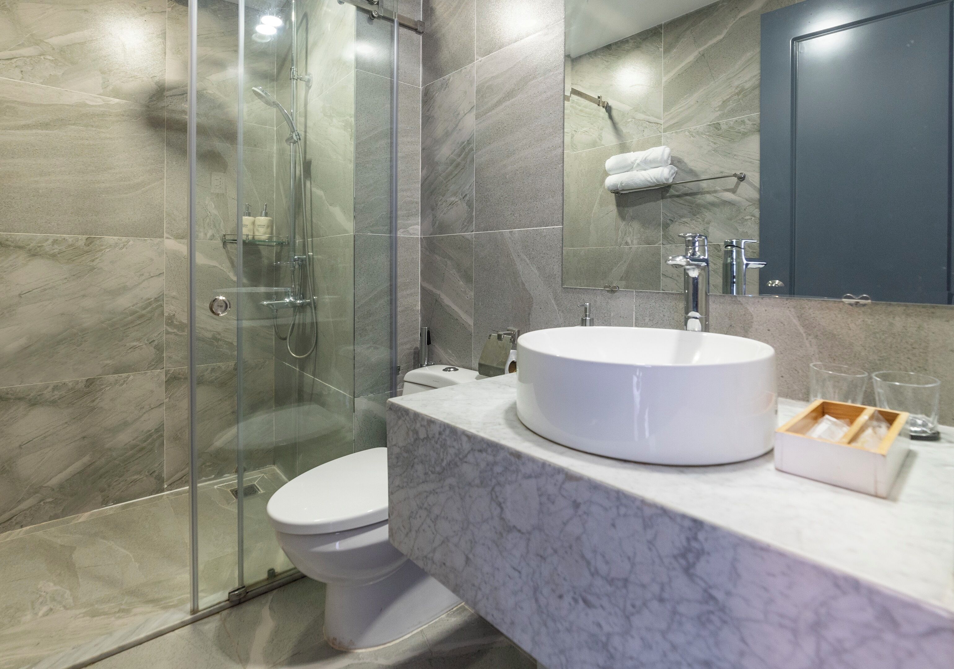 A modern bathroom with a glass-enclosed shower, a white toilet, a marble sink, and a mirror above the sink.