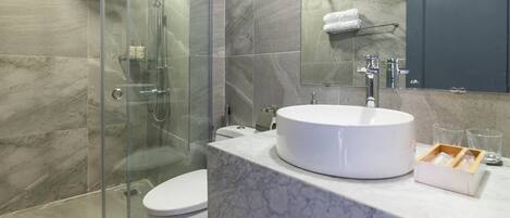 A modern bathroom with a glass-enclosed shower, a white toilet, a marble sink, and a mirror above the sink.