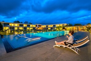 A hotel with a swimming pool, lounge chairs, and a person relaxing by the pool.