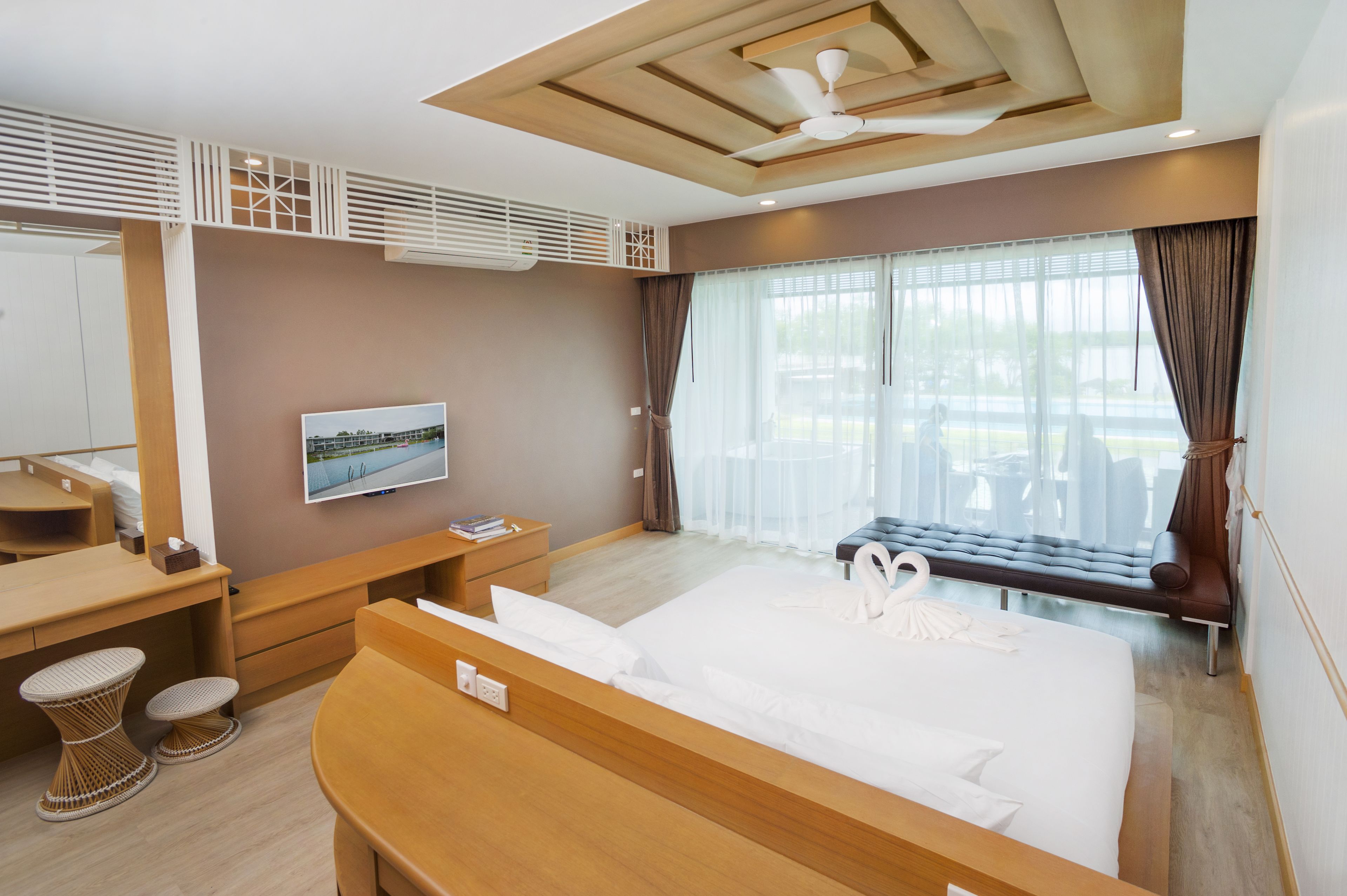 A modern hotel room with a large bed, a desk, a chair, a small table, a bench, and a TV mounted on the wall.