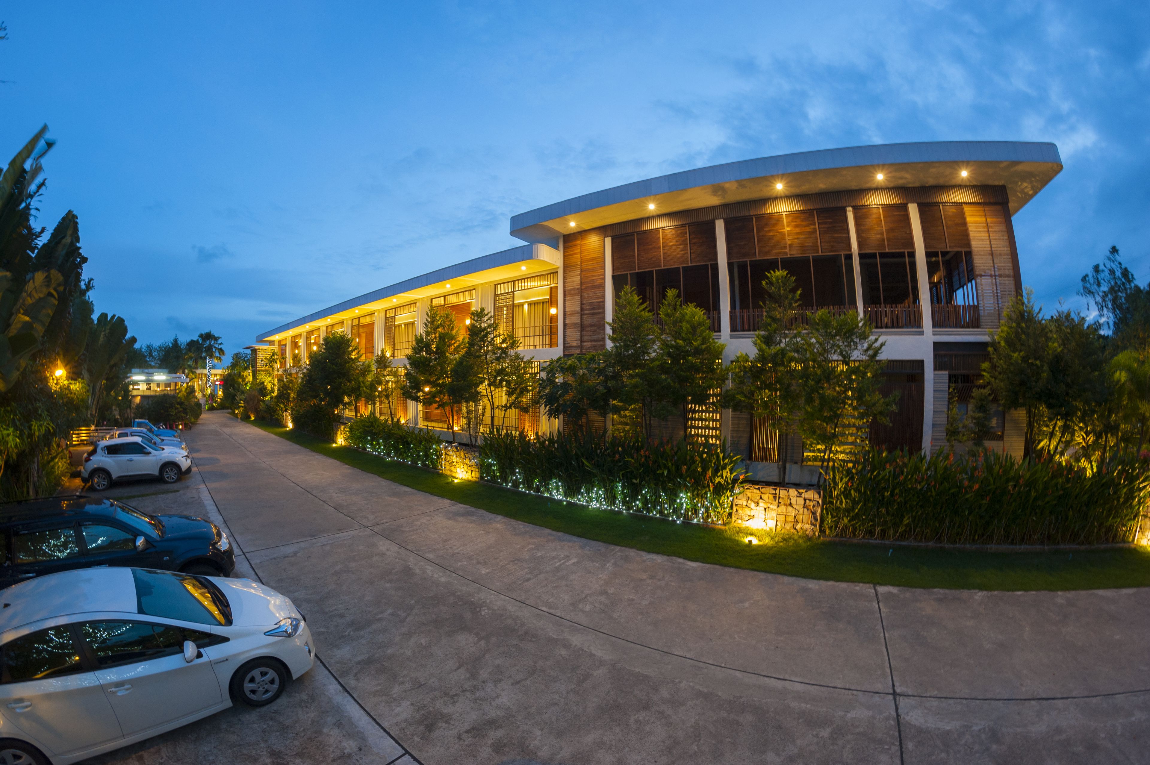 A modern building with a curved facade, a parking area with several cars, and well-maintained landscaping.
