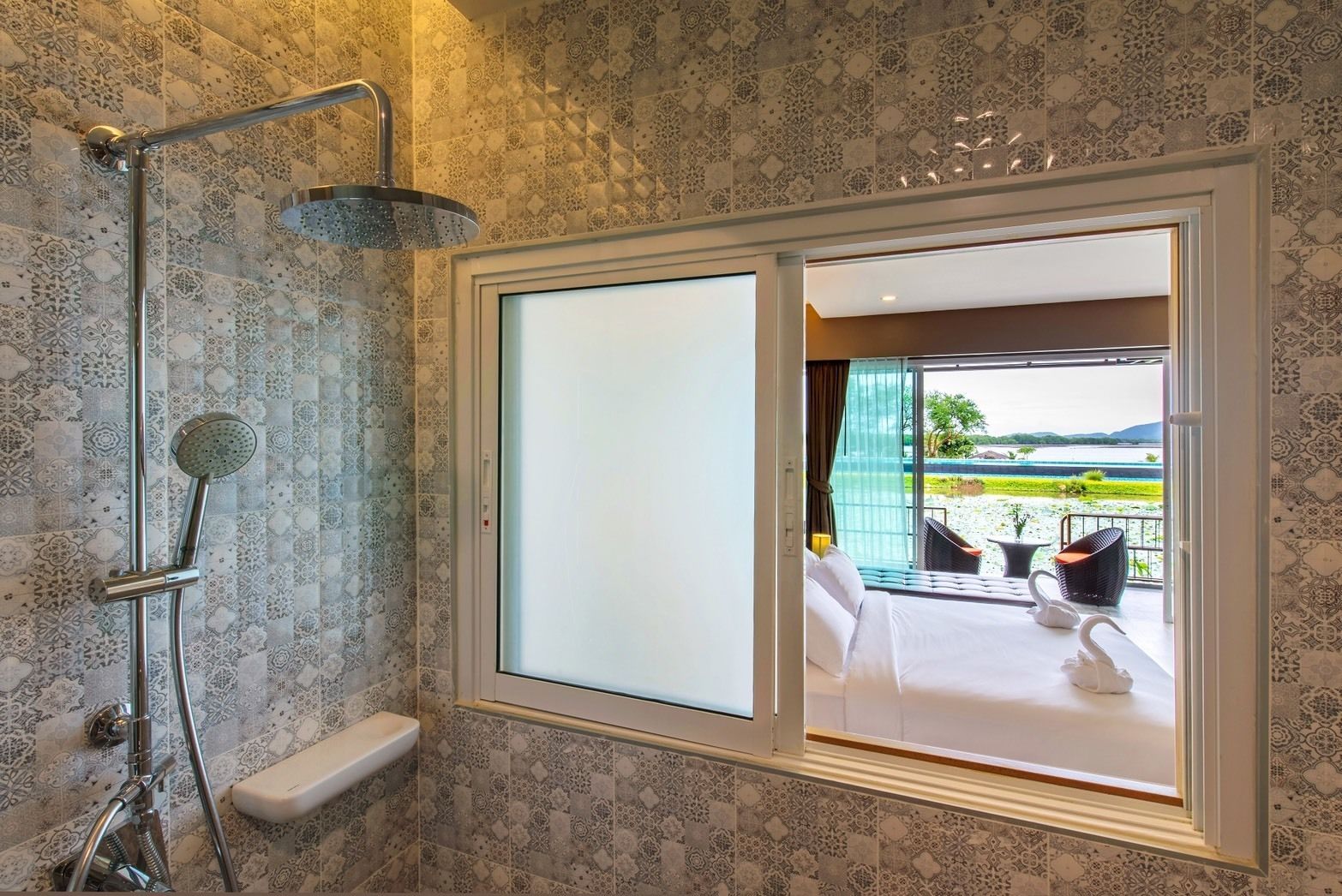 A bathroom with a shower, a toilet, and a large window with a view of a balcony and outdoor area.