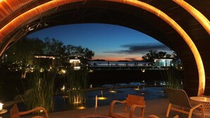 An outdoor seating area with a view of a bridge and water body at dusk. - Baan Rim Ao (Chanthaburi)