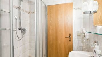 A bathroom with a glass shower enclosure, a wooden door, a sink with a mirror, and toiletries on the wall.