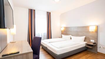 Ein Hotelzimmer mit Bett, Schreibtisch, Stuhl, Fernseher und einem Fenster mit Vorhängen.