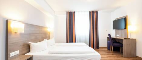 A hotel room with a bed, bedside tables, a desk with a chair, a television, and curtains.