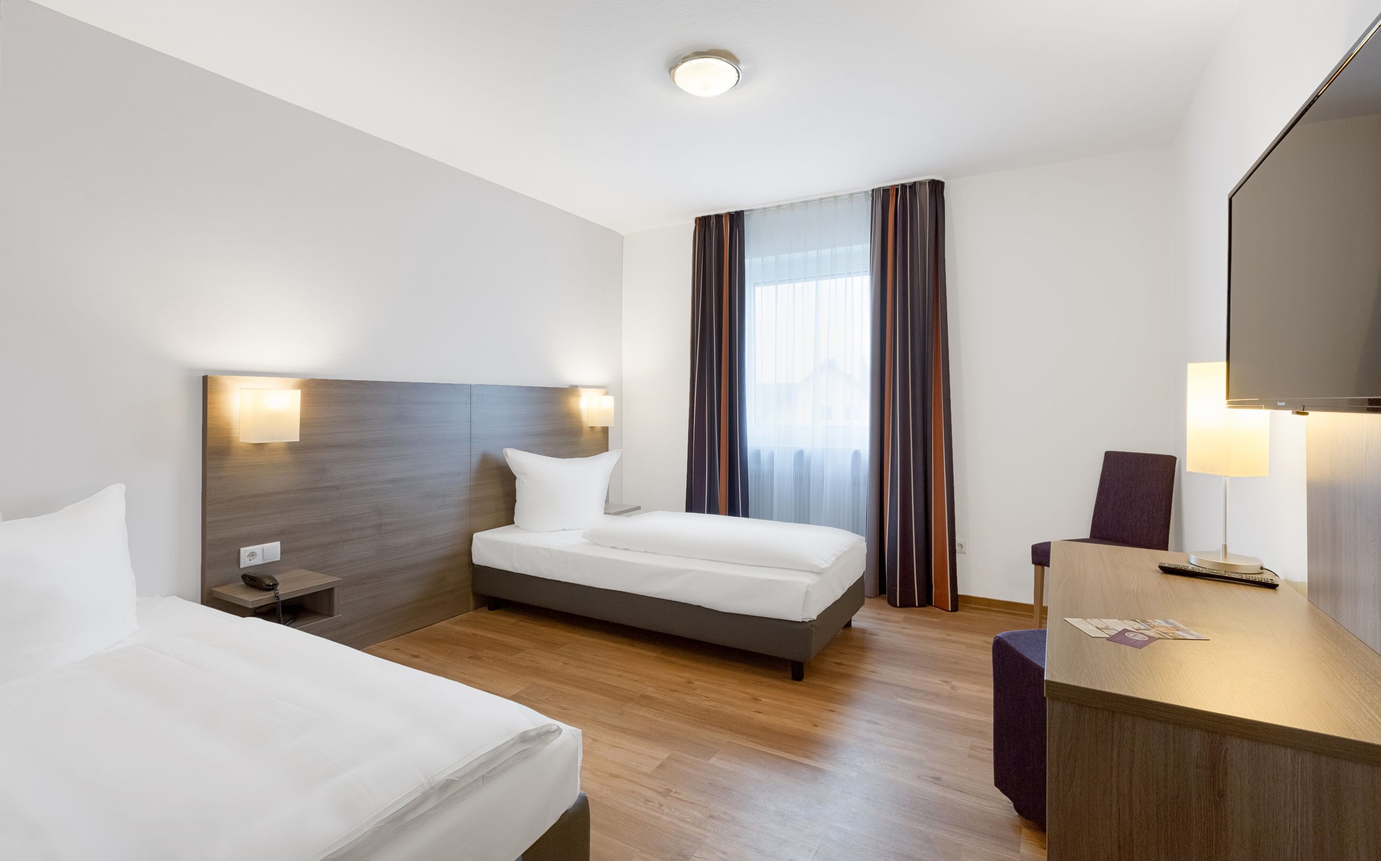 Habitación de hotel con dos camas, un escritorio con silla, un televisor y una ventana con cortinas.