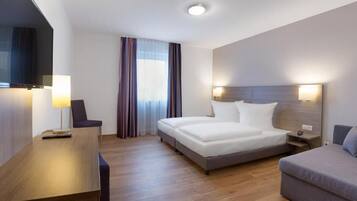 A hotel room with a bed, a desk, a chair, a sofa, a TV, and a window with curtains.