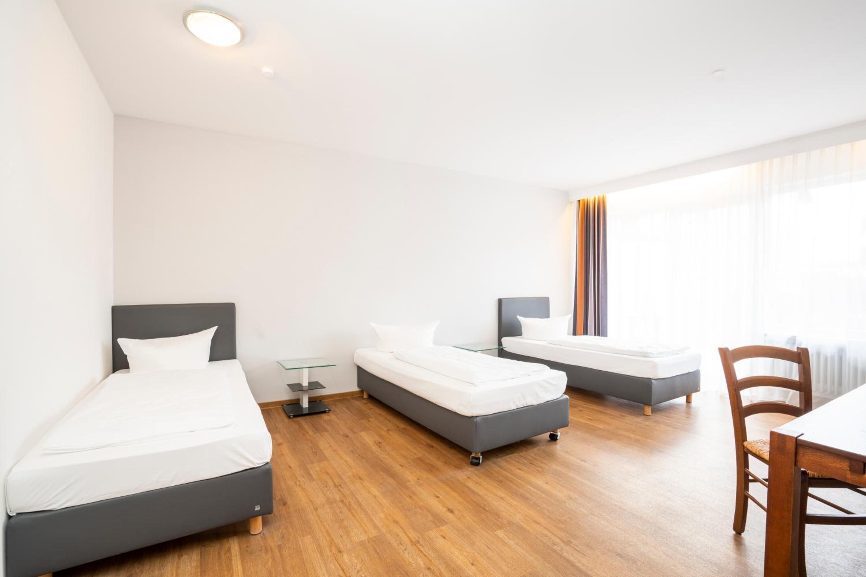 Una camera d'albergo moderna con due letti singoli, un tavolino e una sedia.