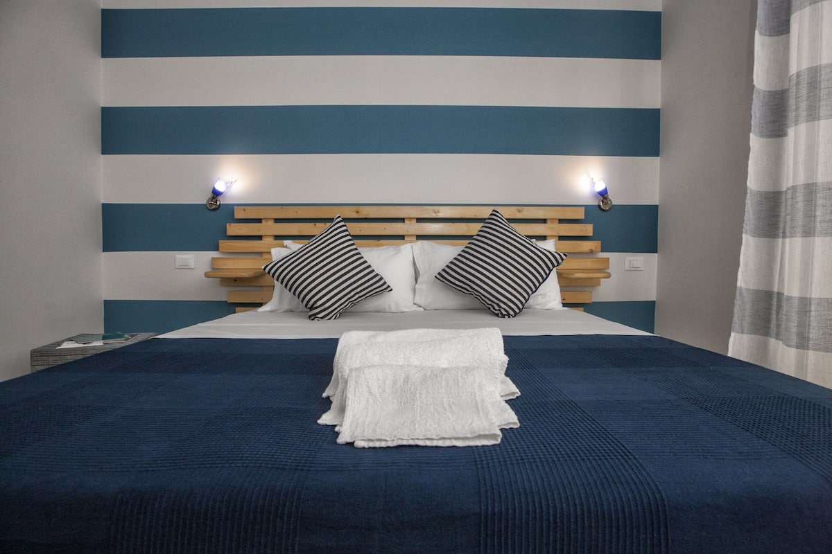 A neatly made bed with striped pillows and a folded white towel, set against a wall with horizontal blue and white stripes.