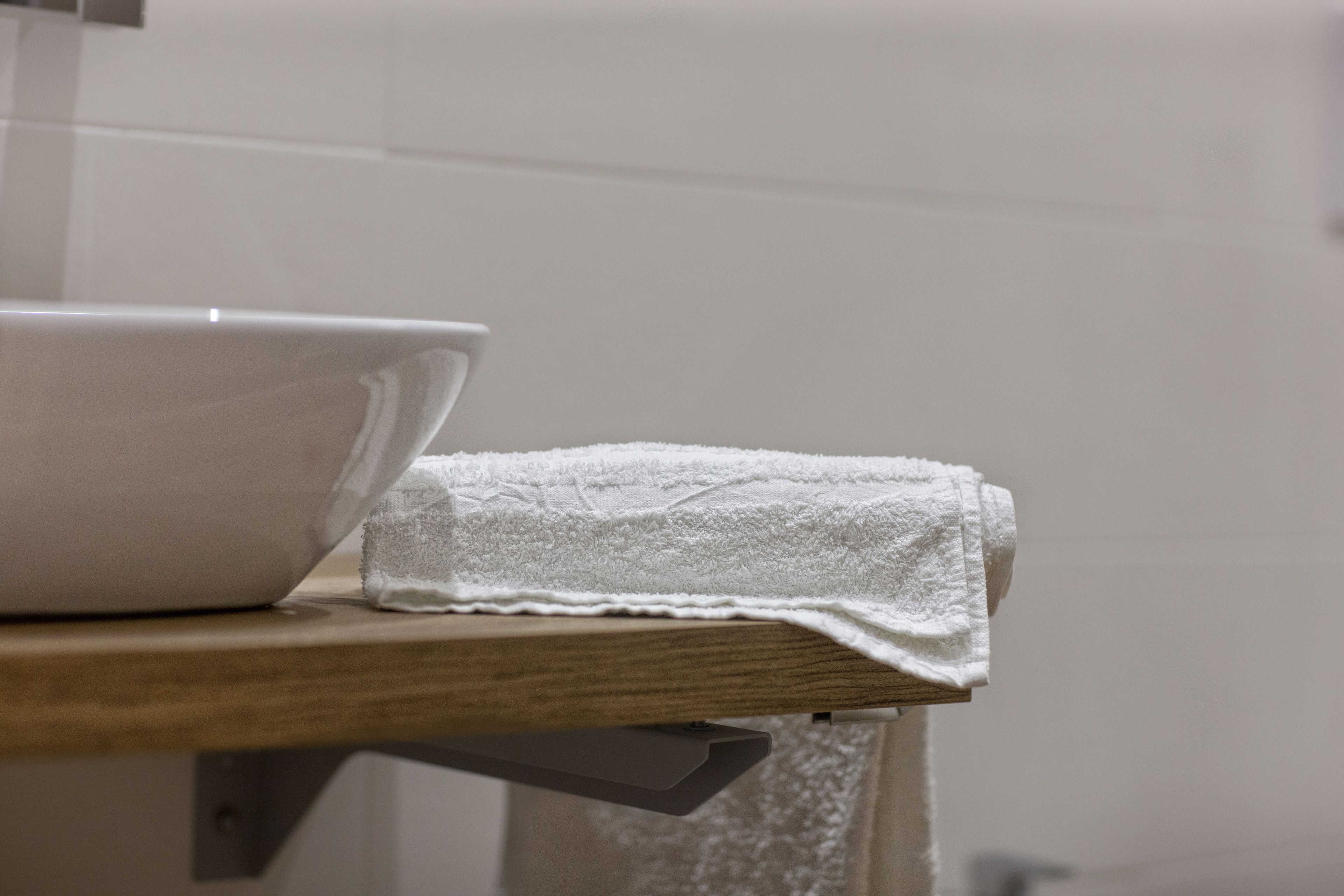 Un cuenco blanco y una toalla doblada sobre un estante de madera en un baño.