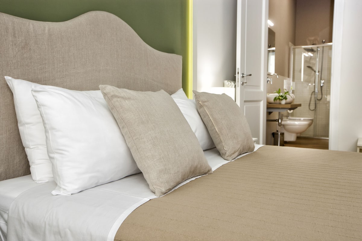 A neatly made bed with a headboard, white and beige pillows, and a beige bedspread.