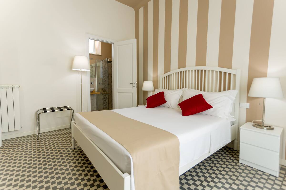 A hotel room with a bed, bedside tables, a radiator, and a checkered floor pattern.