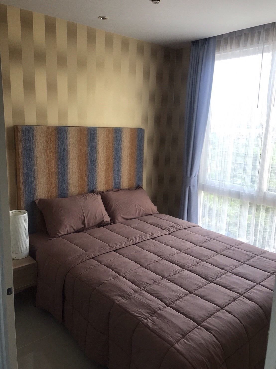 A modern bedroom with a large bed, a headboard with a striped pattern, and a window with sheer curtains.